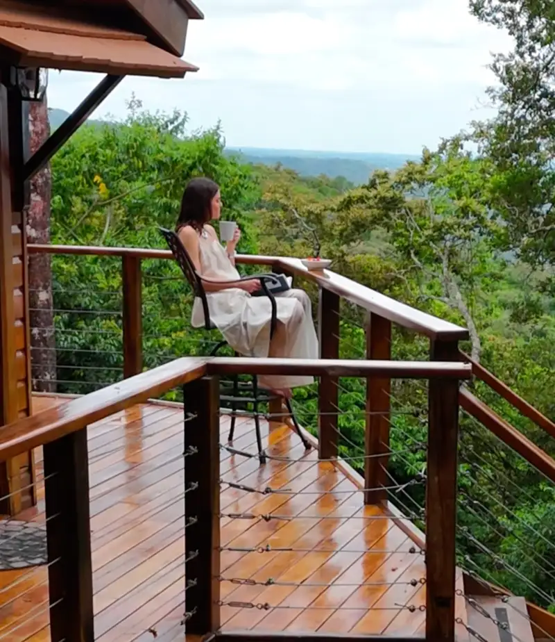 Un huésped toma café en la terraza de una treehouse con vistas al bosque nuboso